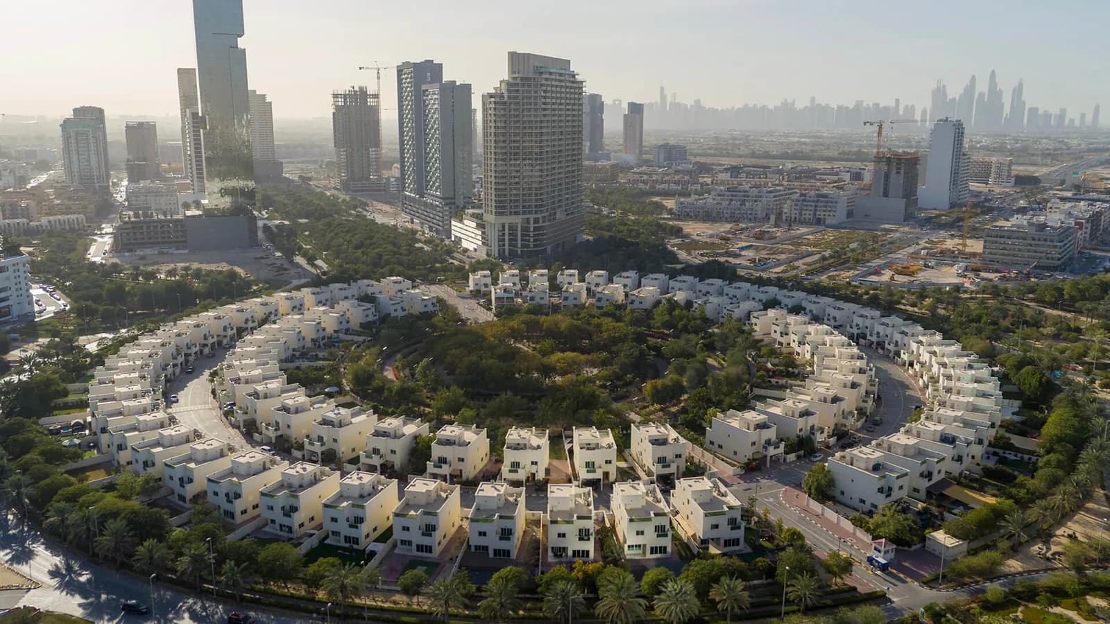 Curving rows of villas around the central park in Jumeirah Village Circle with the Dubai skyline behind