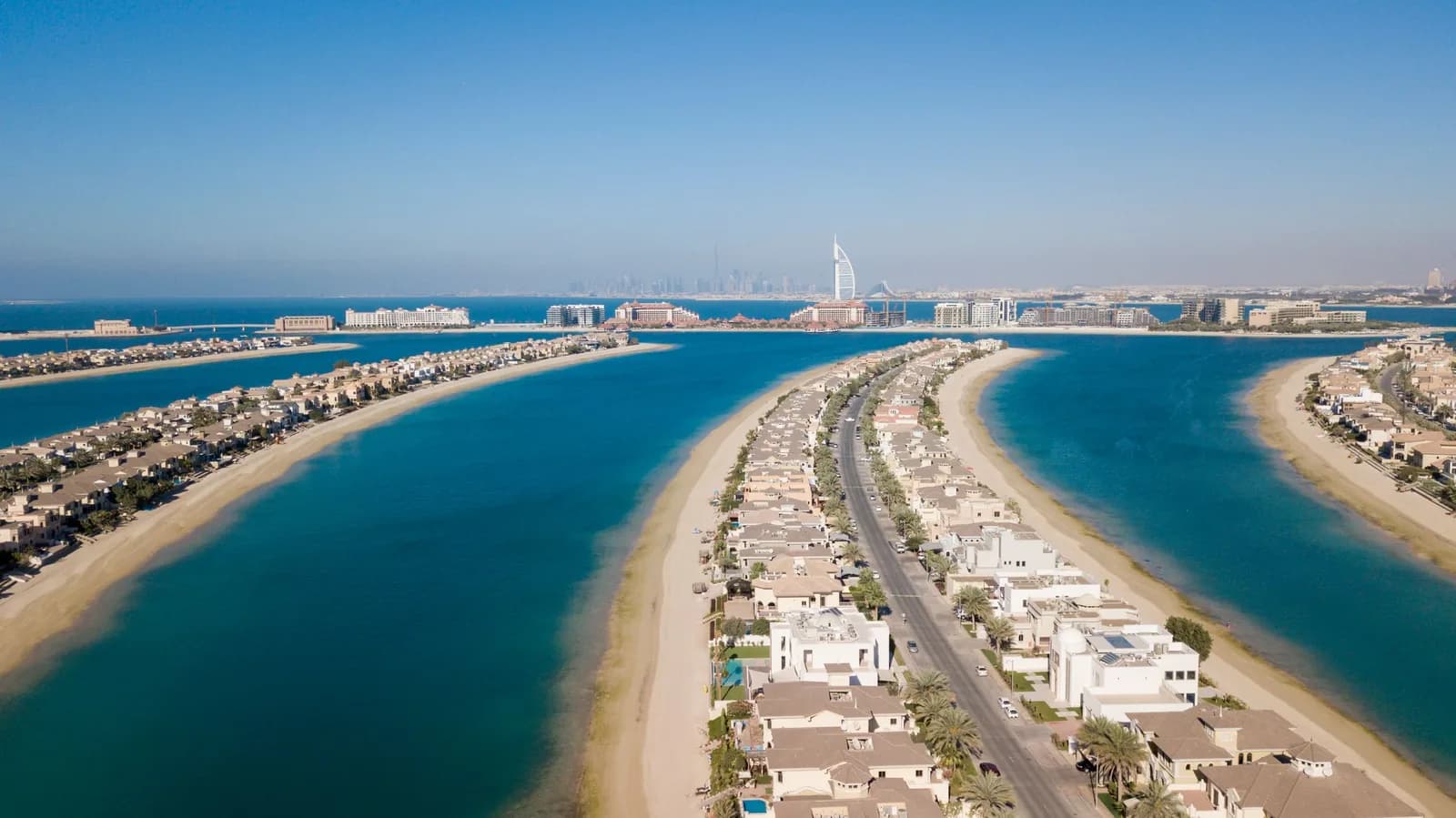 Aerial view of a Palm Jumeirah frond with white villas and the Burj Al Arab on the horizon